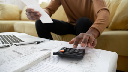 Black small business owner making calculations at home. Close up of african american man checking...