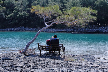 young couple sitting on a bench by the sea