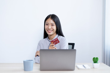 Asian women hold credit cards to shop online on laptops.