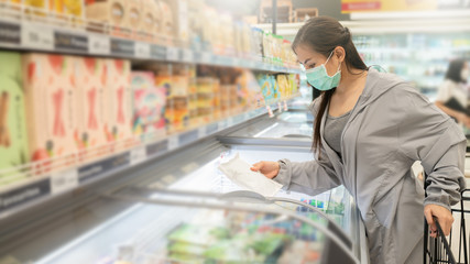 New normal after covid epidemic and shopping concept,young smart Asian woman new lifestyle shoping at supermarket with face shild or mask protection hand choose fresh vegetable as new normal lifestyle