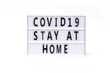 covid 19 stay at home. Text on a vintage lightbox display placed on a white table on a light background. 
