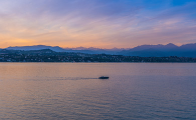 A boat in the sunset with the silhouettes of the mountains in the background on Lake Garda, Italy