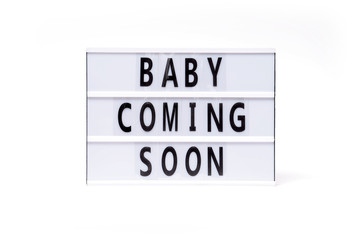 Baby coming soon. Text on a vintage lightbox display placed on a white table on a light background. 