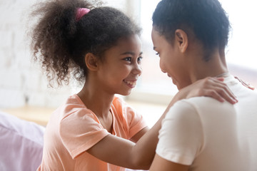 Trusting relations. Affectionate loving black mommy or elder sister and school age girl hugging and looking in eyes of one another, african mom and preteen daughter enjoying happy moments together