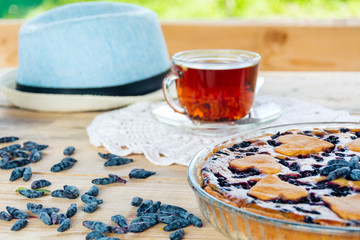 On a wooden table there is a honeysuckle pie and a transparent cup of tea.