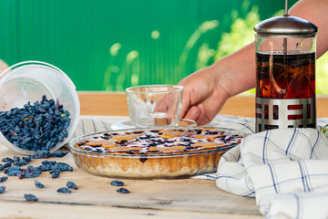 On a wooden table there is a honeysuckle pie and a transparent cup of tea.