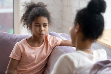 Sharing secrets with mom. Preteen african girl sitting on couch having confident frank talk with understanding mother or elder sister, school psychologist listening to bullying or racial abuse victim