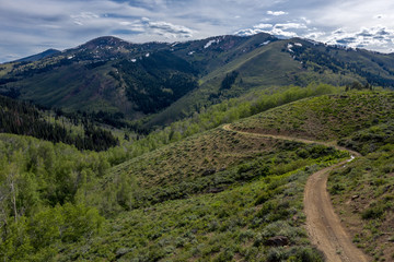 A winding road leading to the horizon and a mountain in the background with snow on the mountain and dramatic clouds in the background, Buck Creek, Jarbidge, Nevada