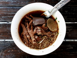 A bowl of noodle soup with chicken drumstick and chicken feet on wooden table