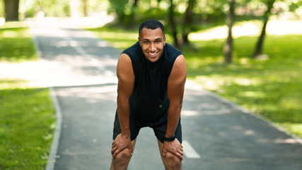 Smiling black jogger resting after marathon run at sunny park