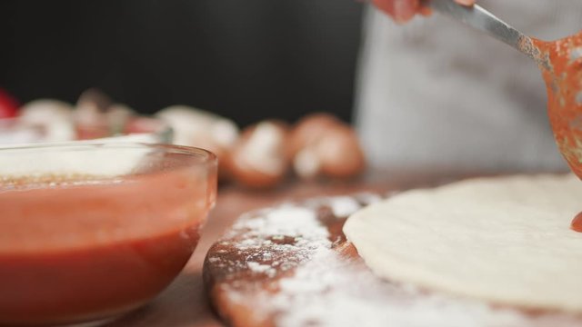 Close-up of chef spreading Tomato Sauce on pizza dough with a ladle in 4K.