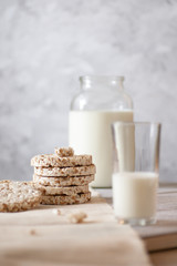 Transparent jar and glass of milk, wholegrain crisp bread on a wooden table on a gray background in a high key