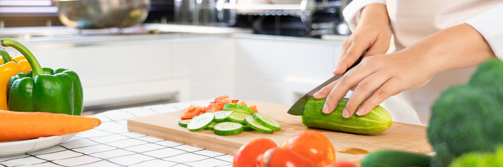 young Asian woman is preparing healthy food vegetable salad by Cutting cucumber for ingredients on cutting board on light kitchen, Cooking At Home and healthy food concept.