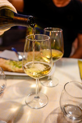 Pouring in glass  cold dry white wine in outdoor cafe at night in Italy