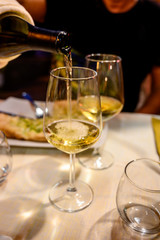 Pouring in glass  cold dry white wine in outdoor cafe at night in Italy