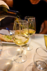 Pouring in glass  cold dry white wine in outdoor cafe at night in Italy
