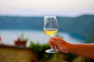 Hand with glass of cold dry white wine served outdoor in cafe at night in Italy