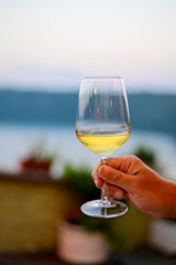 Hand with glass of cold dry white wine served outdoor in cafe at night in Italy