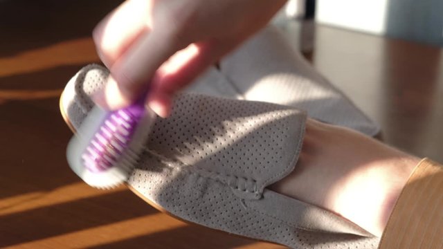 A man cleans light-colored suede shoes with a special brush, closeup
