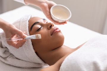 Spa therapist applying face mask for black lady