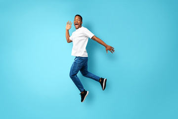 Fototapeta na wymiar African American Guy Shouting Jumping In Air Over Blue Background