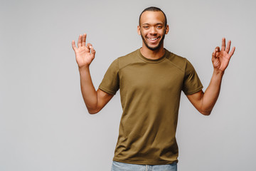 Fototapeta premium Joyful friendly african-american young man in green t-shirt showin og sign gesture over light grey background with copy space