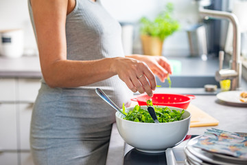 Pregnant woman preparing healthy vegan food in a white salad bowl