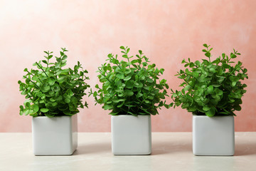 Beautiful artificial plants in flower pots on light marble table against color background