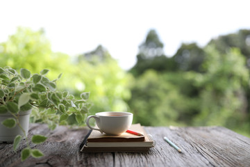 Coffee cup and green plant Peperomia scandens with notebooks and pencil on wooden table