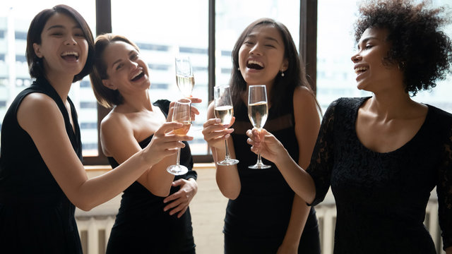 Happy Multiethnic Girls Wearing Elegant Little Black Evening Or Cocktail Dresses Toasting Clinking Holding Champagne Glasses Celebrating Birthday Enjoy Bachelorette Party, Hangout Best Friends Concept