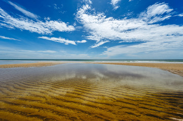 Beautiful white clouds on blue sky over calm sea with sunlight reflection. Midday sky is reflected on water