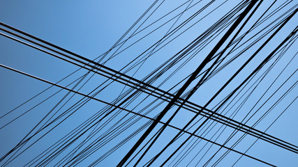 Hundreds of black communication cables crossing with blue sky behind, wire disorder