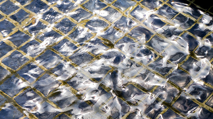 Light reflection on water waves with blue mosaic on the bottom, diagonal lines of the joints, silver effect of the waves vibration
