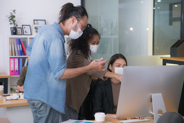 Asian office workers wearing face masks working in new normal office and doing social distancing during corona virus covid-19 pandemic