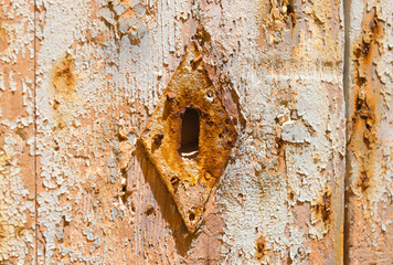 
old rusted keyhole on a weathered light wooden door