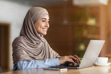 Happy arab woman chatting with clients on laptop