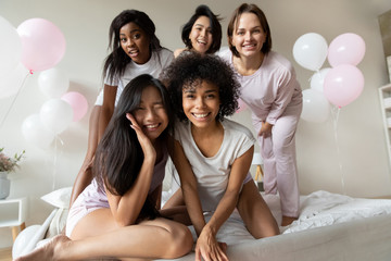 Funny diverse girls in pyjamas posing looking at camera having fun fool around in bed enjoy...