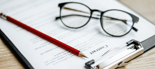 A contract on a wooden work table with glasses and a red pencil. The documents are ready for signing. Business concept. Collaboration agreement.