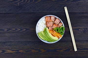 Hawaiian salmon dish with vegetables and rice on dark rustic background. Poke bowl