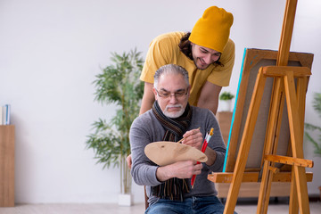 Old man taking lesson from young painter