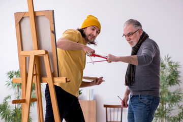 Old man taking lesson from young painter