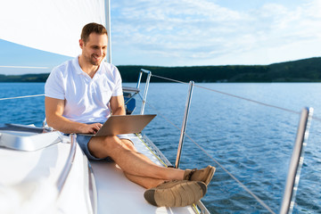 Happy Man On Yacht Sitting With Laptop Working On Sailboat