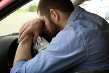 Tired man sleeping on steering wheel in his car