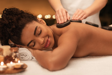 Obraz na płótnie Canvas African lady receiving professional hot stone massage at spa