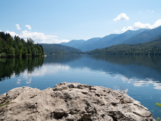 View towards reflecting lake with forest to the left and mountains to the right with rock surface...