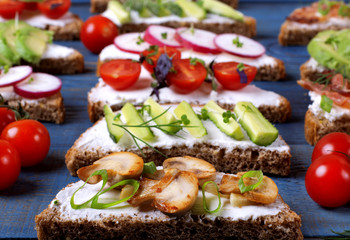 Bruschetta assortment with cream cheese, vegetables, mushrooms and bacon served on the blue wooden table. Traditional Italian antipasto with various toppings