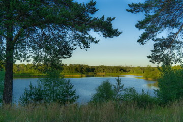 Fototapeta na wymiar Lake view between trees. Evening landscape