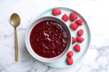 Delicious jam and fresh raspberries on white marble table, flat lay