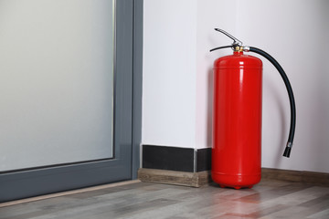 Obraz premium Fire extinguisher near door indoors. Space for text