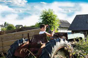A 10-year-old school-age boy tries to start an old tractor or car. Repair. Little helper. Harvest...